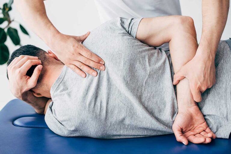 A middle-aged person sits comfortably on a living room sofa, drinking water and gently stretching their back.