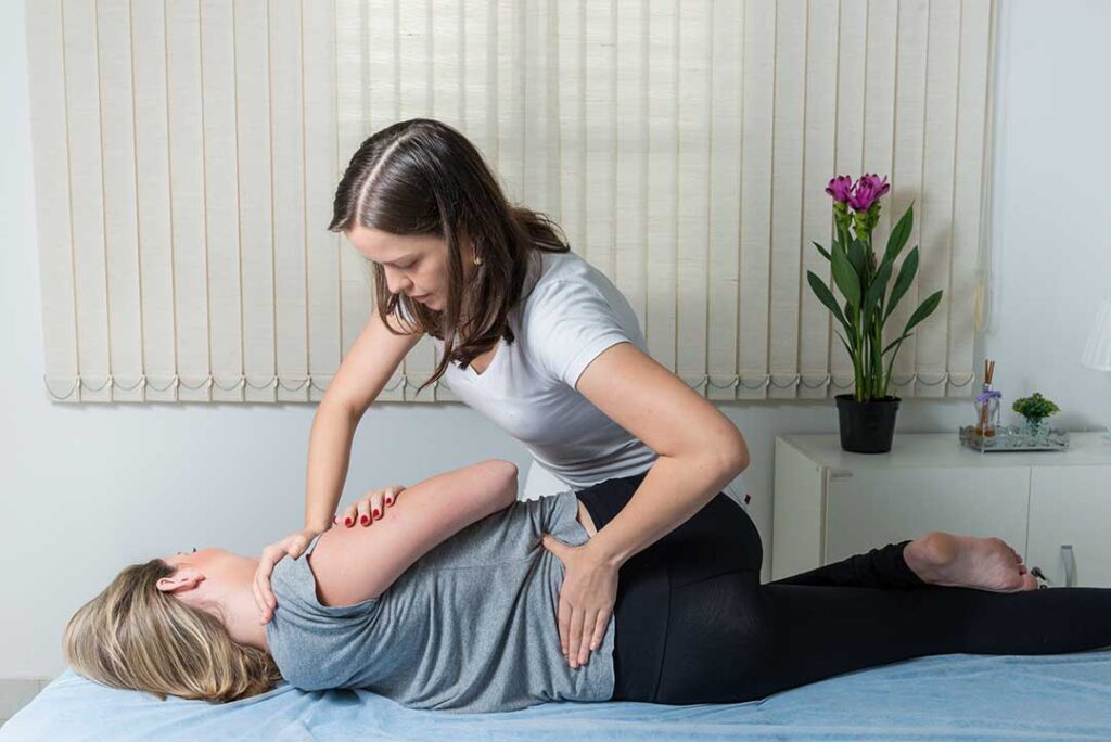 Person adjusting a laptop at an ergonomic desk while gently stretching the neck and shoulders